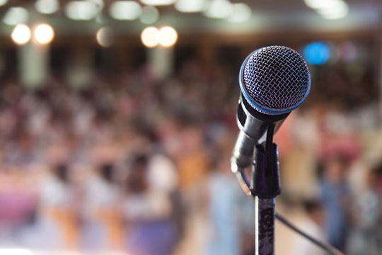 A microphone stand on a stage in front of an audience. A microphone stand on a stage in front of an audience.