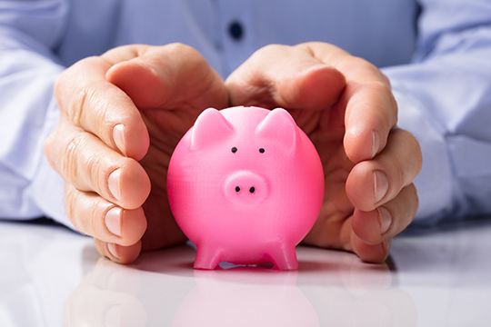 Hands protecting a piggy bank.