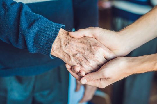 Proche aidante tenant les mains d’une personne âgée.