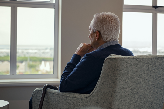La solitude : « une menace urgente pour la santé » Homme assis sur une chaise, regardant pensivement par la fenêtre.