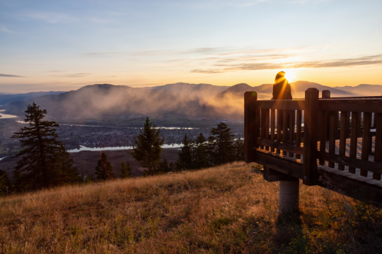Adult woman standing at a lookout with a view of Kamloops, British Columbia.