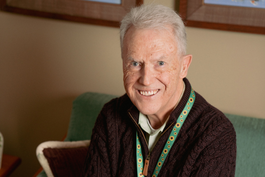 im Mann sourit et il est assis sur un fauteuil vert.