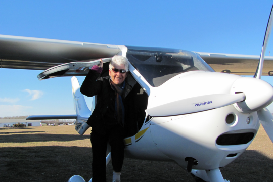 Barbara Biddle received the Queen’s Platinum Jubilee medal. Barbara Biddle sitting in the doorway of a single-engine aircraft.