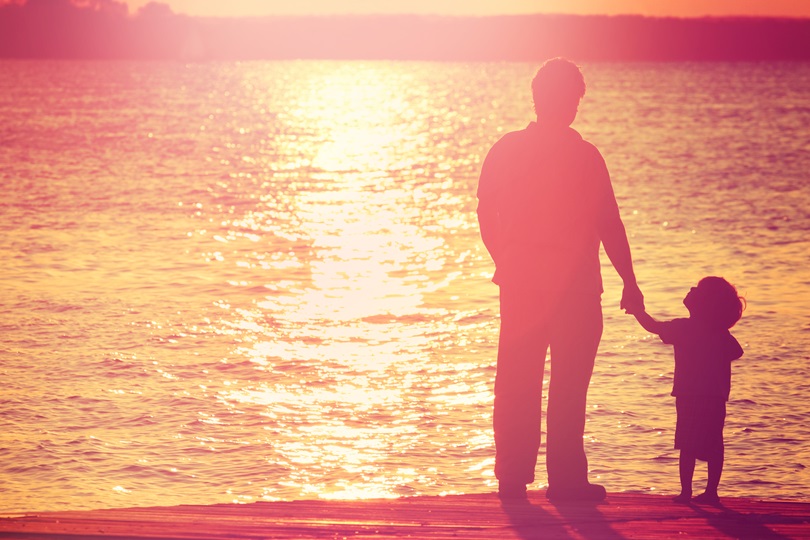 Père et fils sur un quai au coucher du soleil, garçon regardant son père.