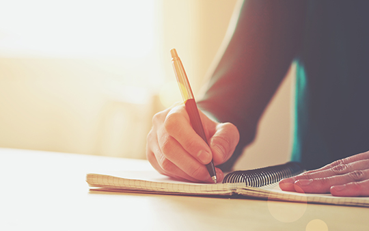 Hand with pen writing on notebook.