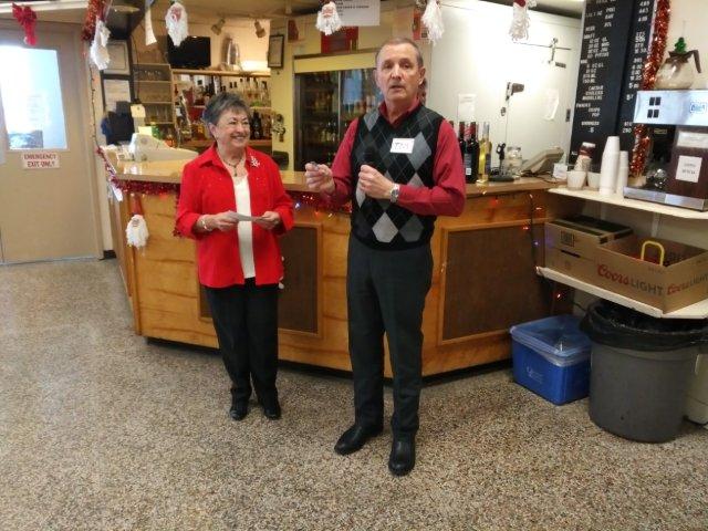 A man reading from a small piece of paper with a smiling woman standing next to him Quintrent Branch president Tom Kupecz announcing giveaway winners