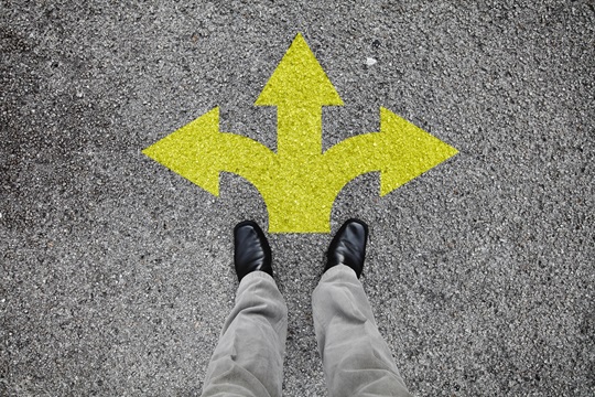 Une paire de pieds debout sur une route goudronnée avec flèche jaune impression pointage dans trois directions différentes pour le concept de prise de décision à la croisée des chemins.