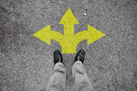 Une paire de pieds debout sur une route goudronnée avec flèche jaune impression pointage dans trois directions différentes pour le concept de prise de décision à la croisée des chemins. Une paire de pieds debout sur une route goudronnée avec flèche jaune impression pointage dans trois directions différentes pour le concept de prise de décision à la croisée des chemins.
