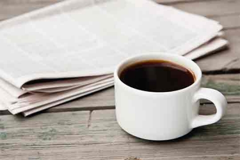 A newspaper and a cup of coffee on a table. A newspaper and a cup of coffee on a table.