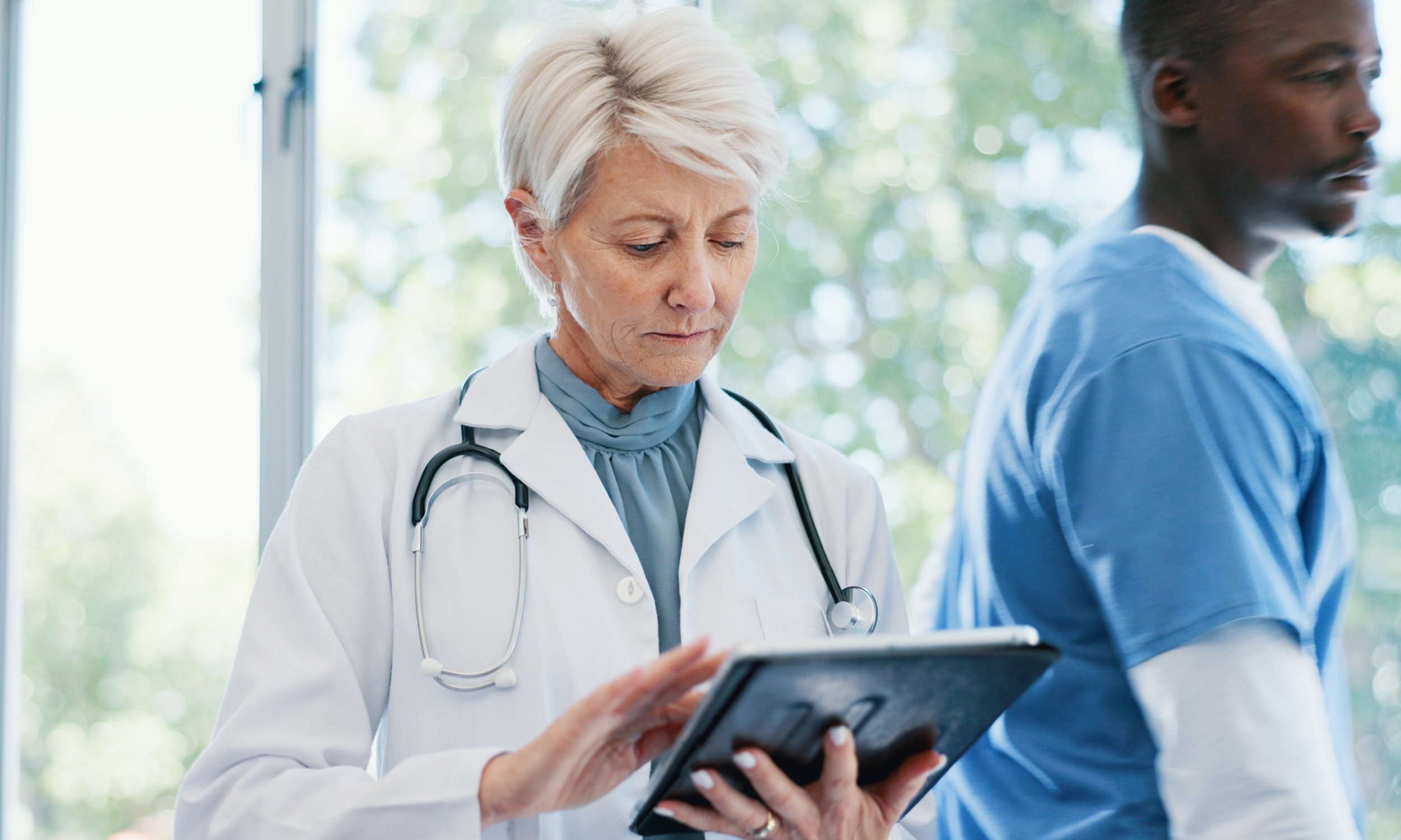 Physician [AJ7.1]reviewing information on a tablet in a health-care setting.
