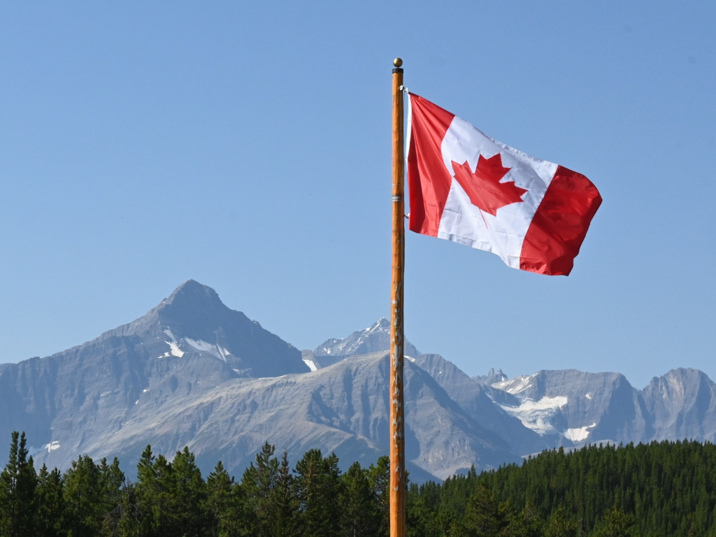 Canadian flag flying in the foreground of a mountain scape.