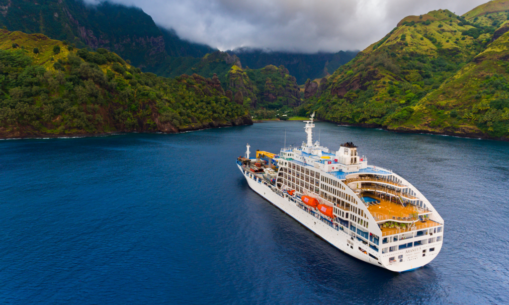 Aranui 5, a passenger and cargo ship, sailing into the harbour at Fatu Hiva in French Polynesia, surrounded by steep green mountains.